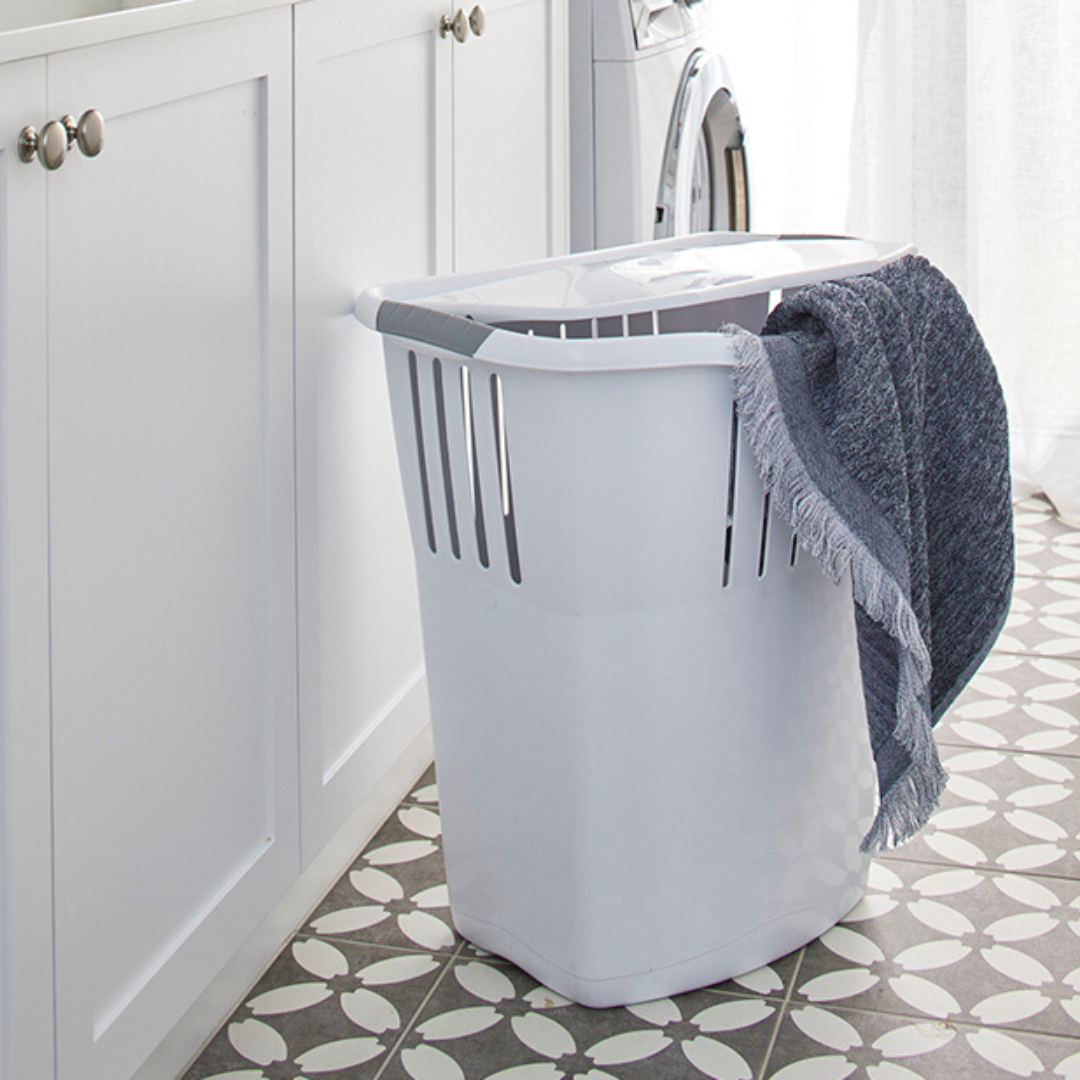 white plastic laundry hamper in laundry with towels hanging out over side of hamper.